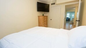 A bedroom with a bed, a dresser, a television mounted on the wall, and an open door leading to another room. - 2br Ground Floor, Sleeps 8, Pets Ok - Spi 2 Bedroom Apts (South Padre Island)