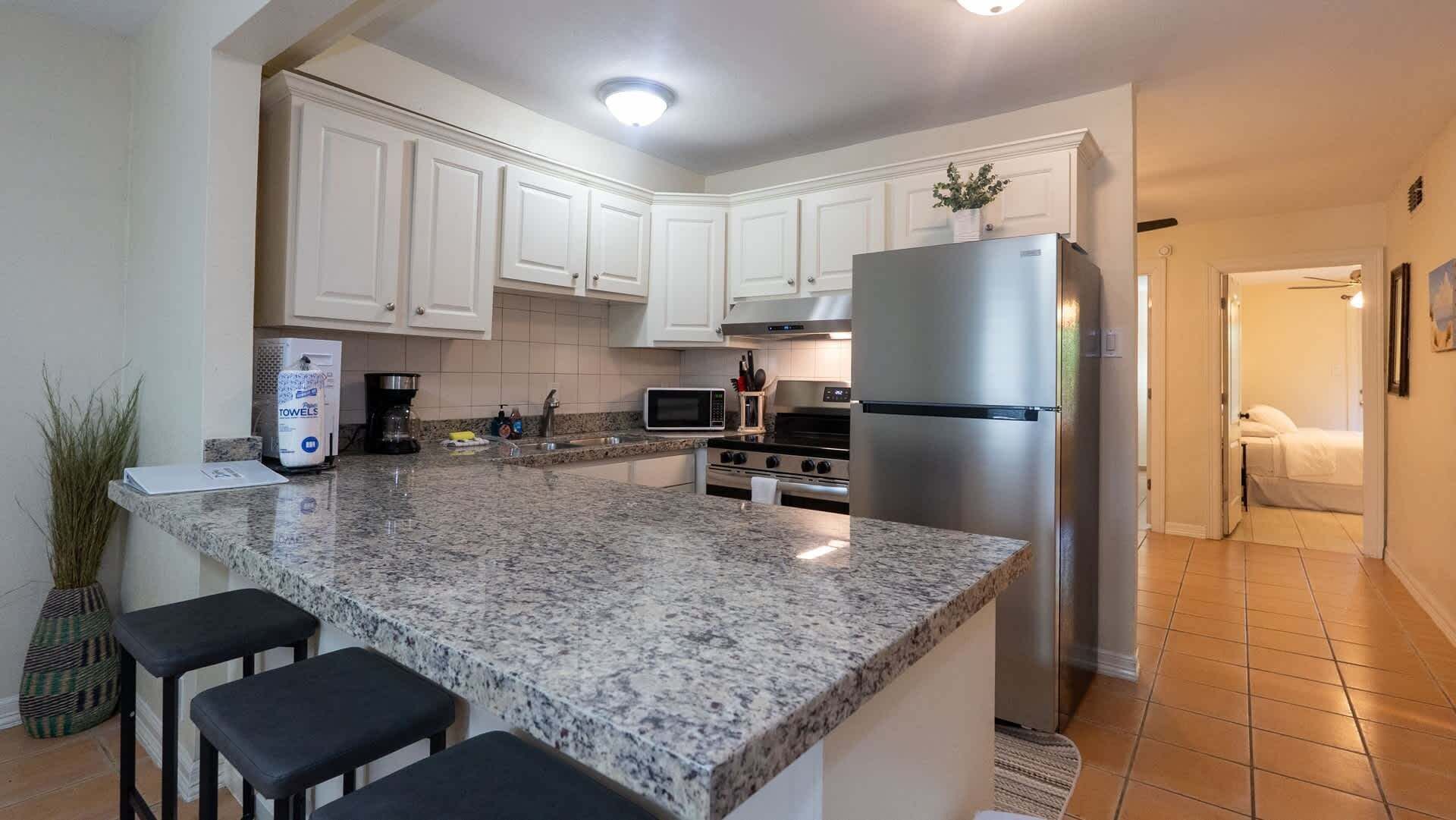 A modern kitchen with white cabinets, granite countertops, a stainless steel refrigerator, and a microwave.