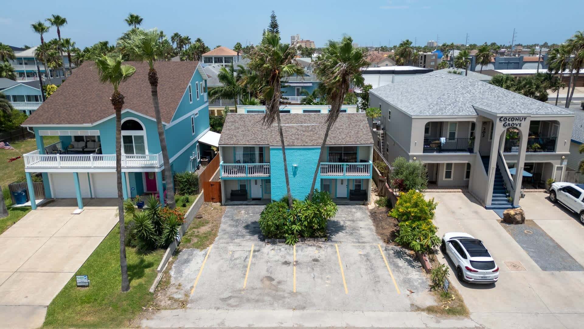 Une propriété située en bord de mer, comprenant plusieurs bâtiments à étages, un espace de stationnement et une voiture blanche garée sur le parking.