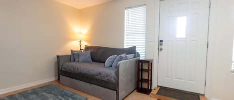 A living room with a sofa, a lamp, a door, and a small table.