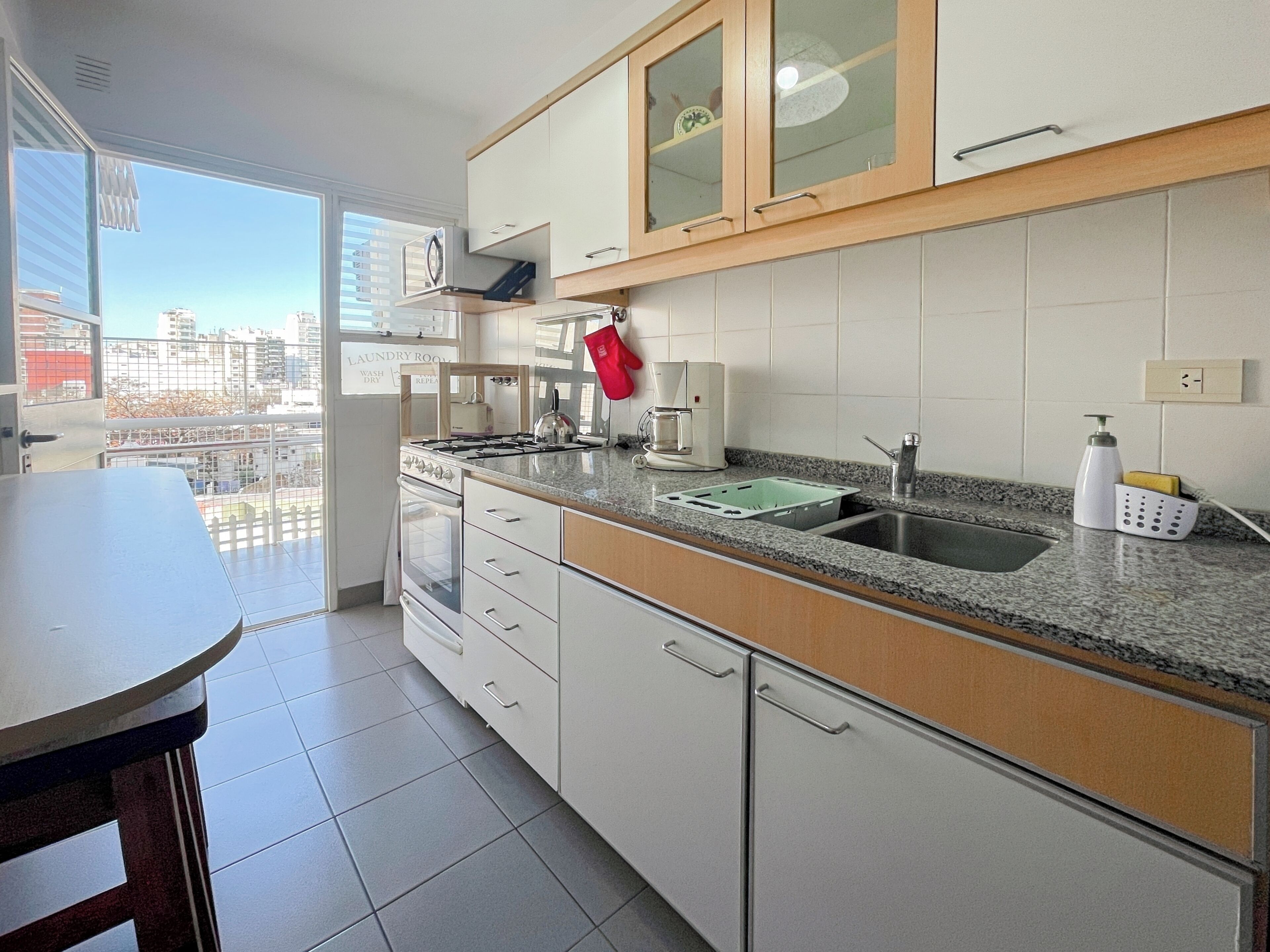 A modern kitchen with white cabinets, a granite countertop, a gas stove, a coffee maker, and a view of the city through large windows.