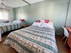 Quarto de hotel com duas camas, uma escrivaninha e uma cadeira.