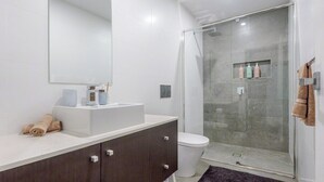 Une salle de bain moderne avec un lavabo blanc, un meuble sombre et une cabine de douche en verre.