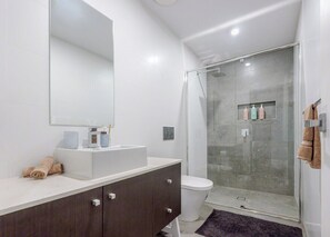 A modern bathroom with a white sink, dark cabinet, and a glass shower enclosure. - Trinitus | Mountain View | Parking | Central (Wollongong)