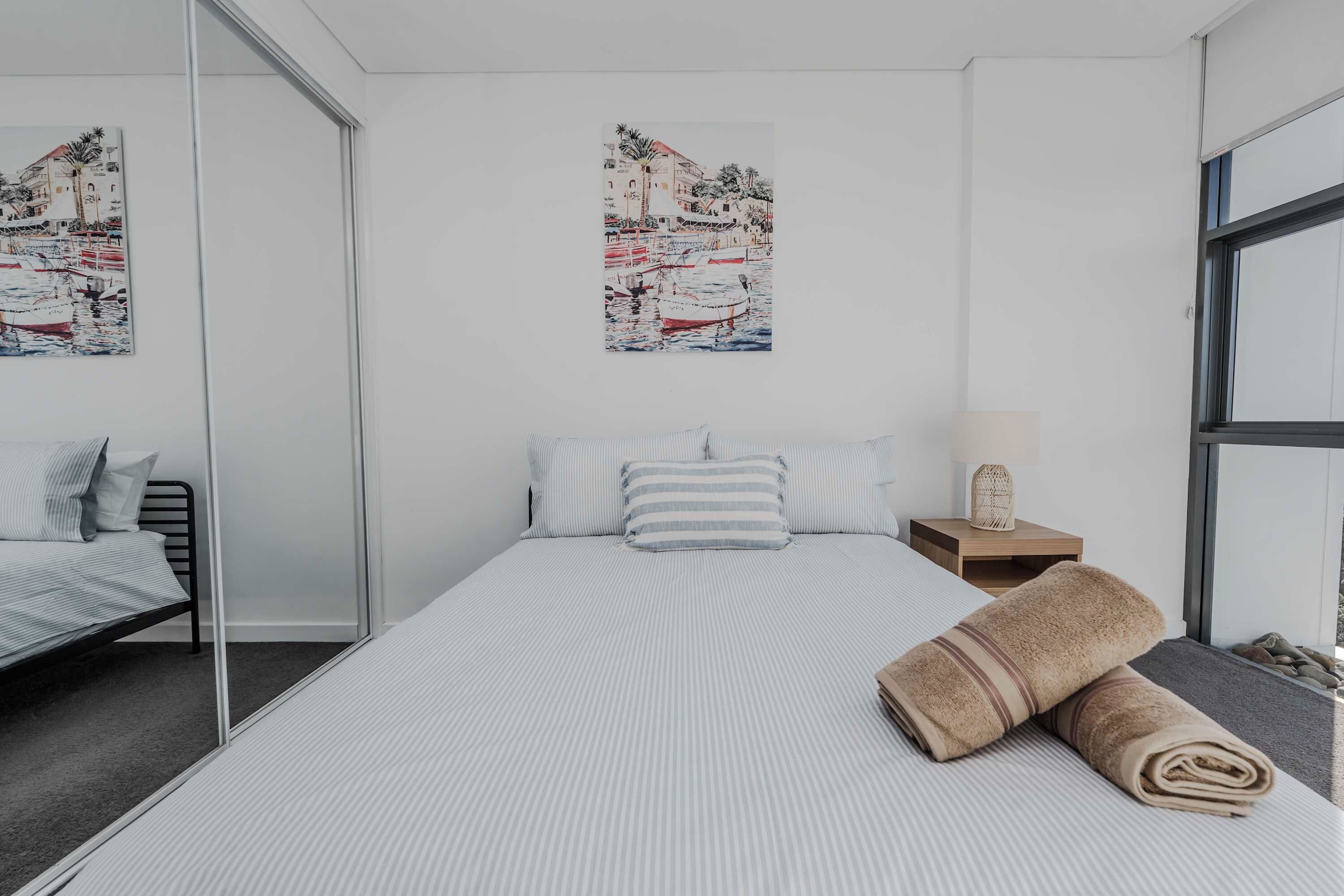 Een hotelkamer met een bed, een nachtkastje, een lamp, een spiegel en twee kunstwerken aan de muur.