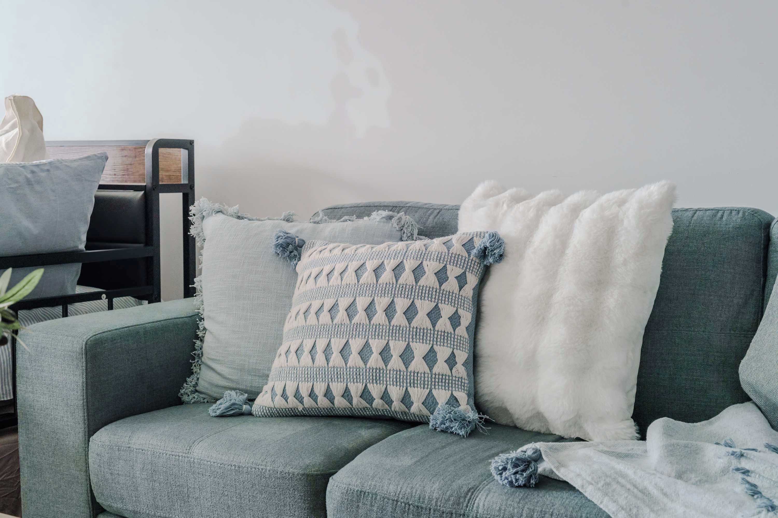 Un salon moderne avec un canapé gris, un coussin décoratif à motifs et un plaid blanc et moelleux.