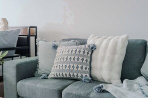 A modern living room with a grey sofa, a patterned throw pillow, and a white fluffy throw. - Trinitus | Mountain View | Parking | Central (Wollongong)
