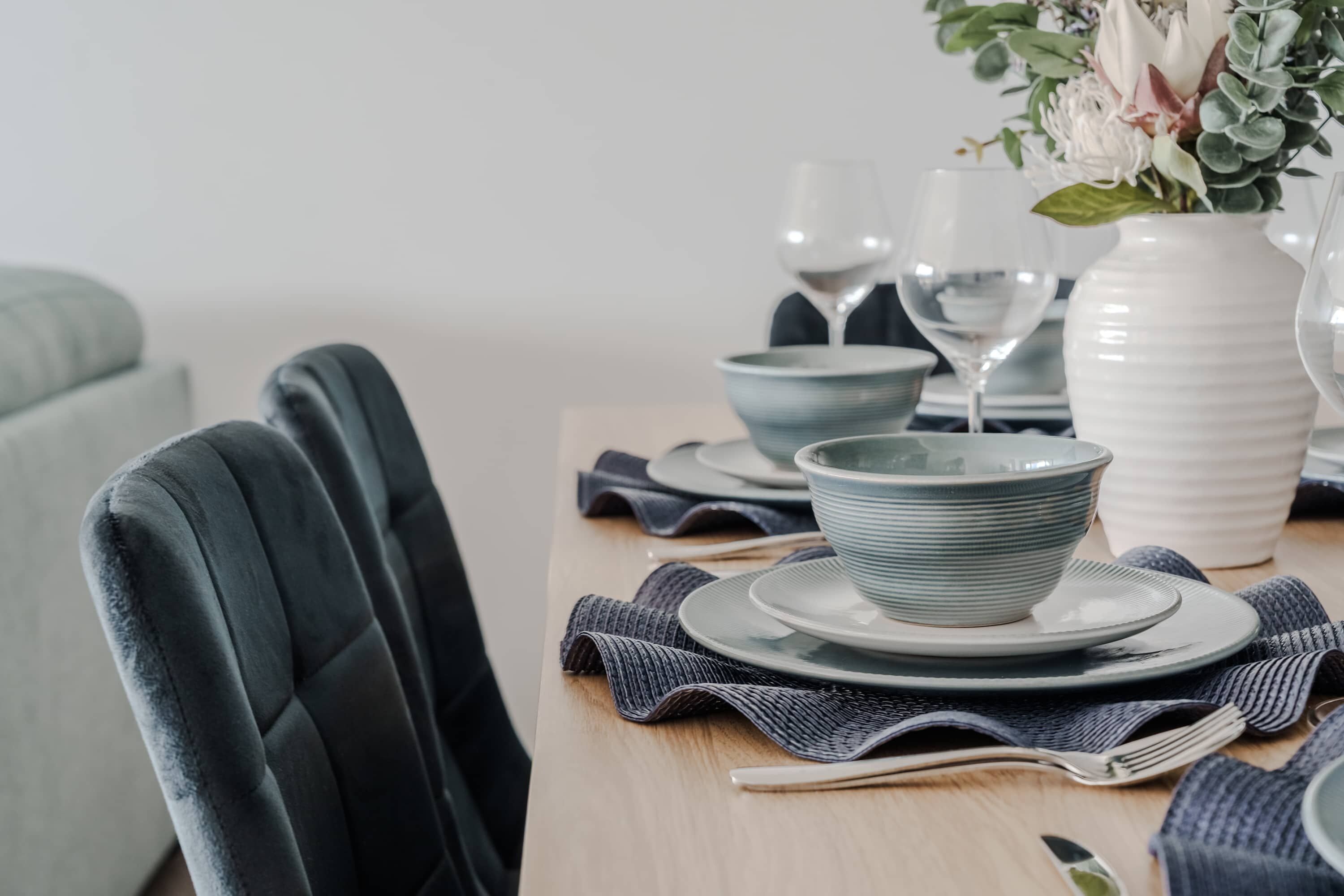 Une table à manger dressée avec des assiettes, des bols et un vase rempli de fleurs.