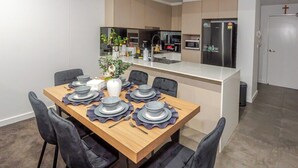 Une cuisine moderne avec un îlot central, une table à manger dressée avec des assiettes et des couverts, et des chaises noires.