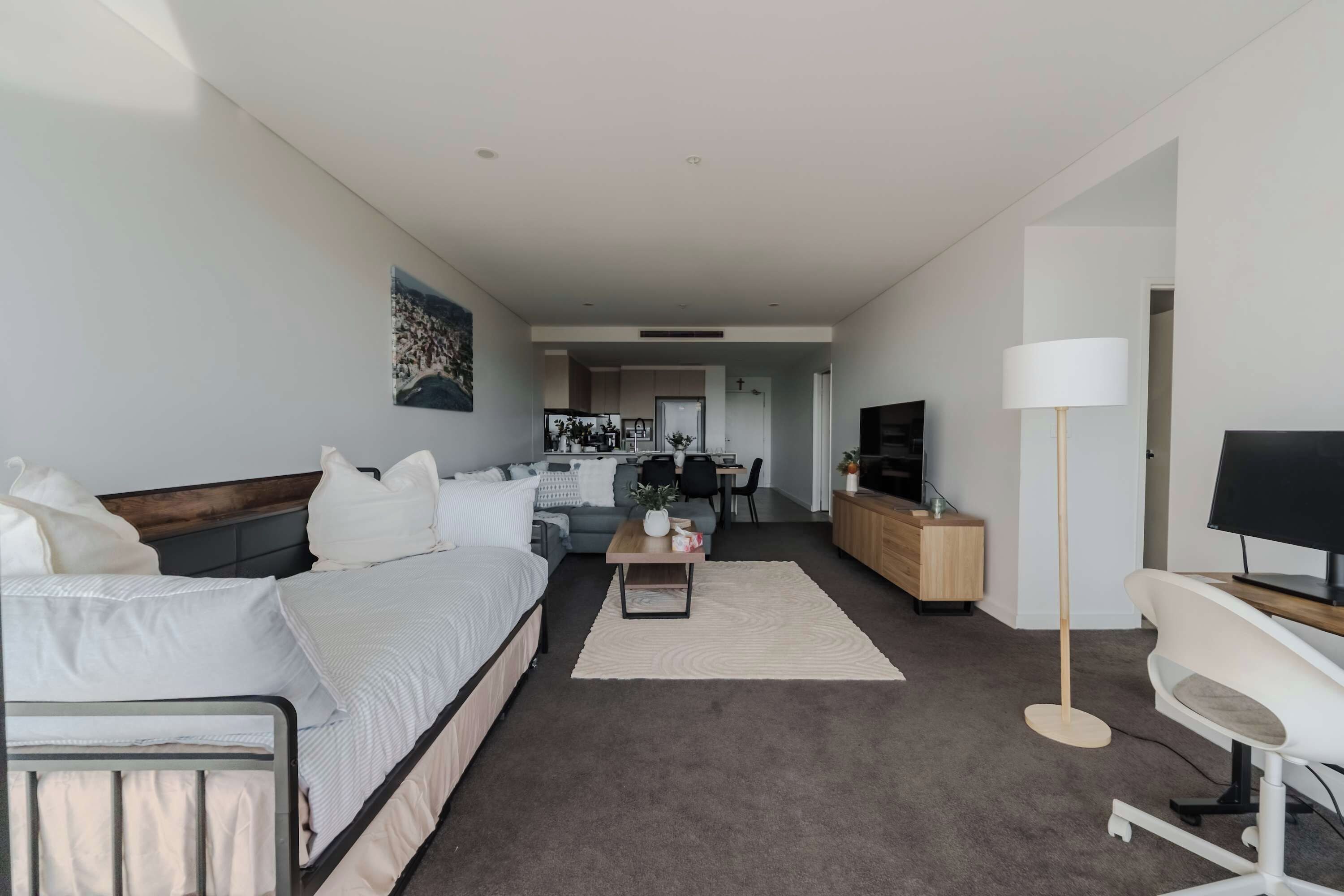 Een moderne hotelkamer met een bed, een bank, een bureau, een televisie en een keuken in de achtergrond.