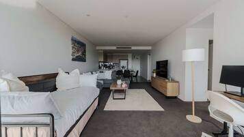 Een moderne hotelkamer met een bed, een bank, een bureau, een televisie en een keuken in de achtergrond.