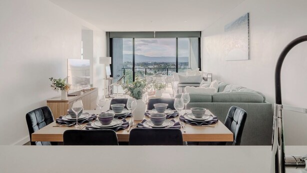 Un espace repas moderne avec vue sur la ville, comprenant un canapé et une table à manger dressée pour quatre personnes.