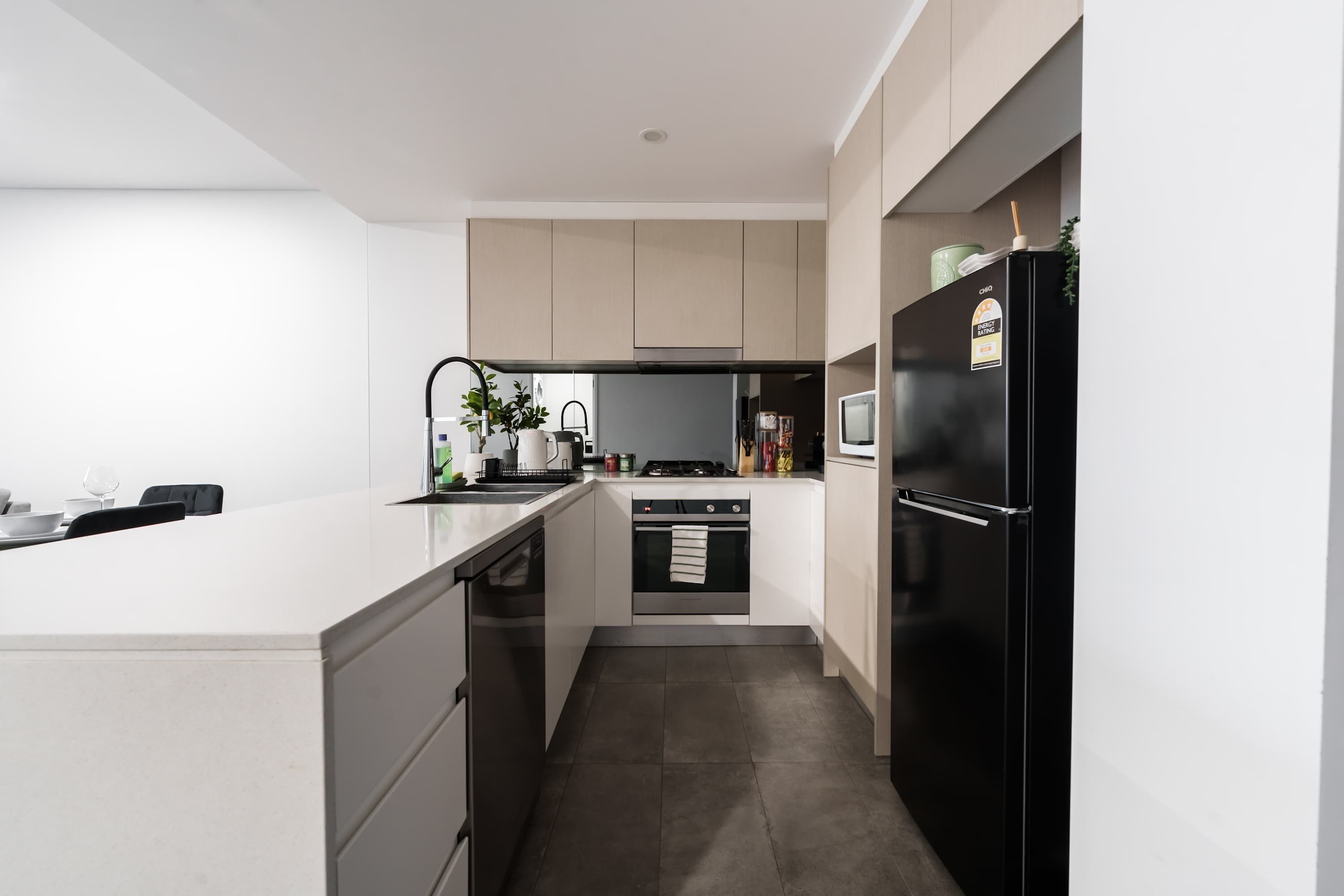 A modern kitchen with a central island, built-in oven, and a black refrigerator.