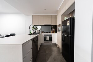 A modern kitchen with a central island, built-in oven, and a black refrigerator. - Spiritus | Mountain View | Parking | Central (Wollongong)