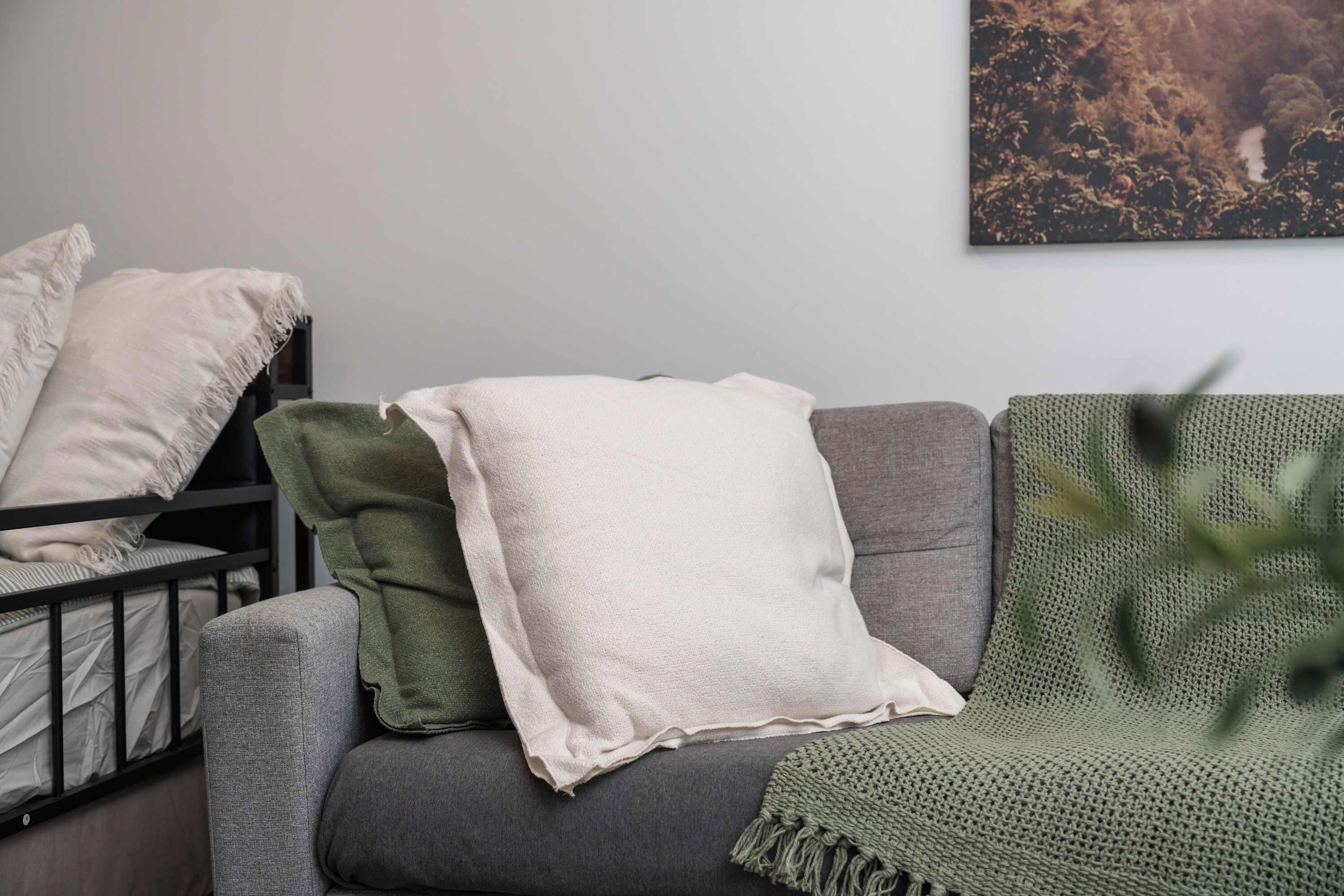 A grey sofa with a white throw blanket and a green knitted throw.