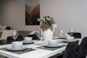 A dining table set with white plates, bowls, and cutlery, with a vase of flowers in the center. - Spiritus | Mountain View | Parking | Central (Wollongong)