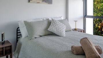 Een net opgemaakt bed met een grijs beddekleed met patroon, een wit kussen en een opgerolde bruine handdoek aan de zijkant.