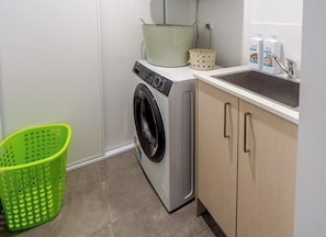 Un área de lavandería con lavadora, un lavabo y una cesta verde.