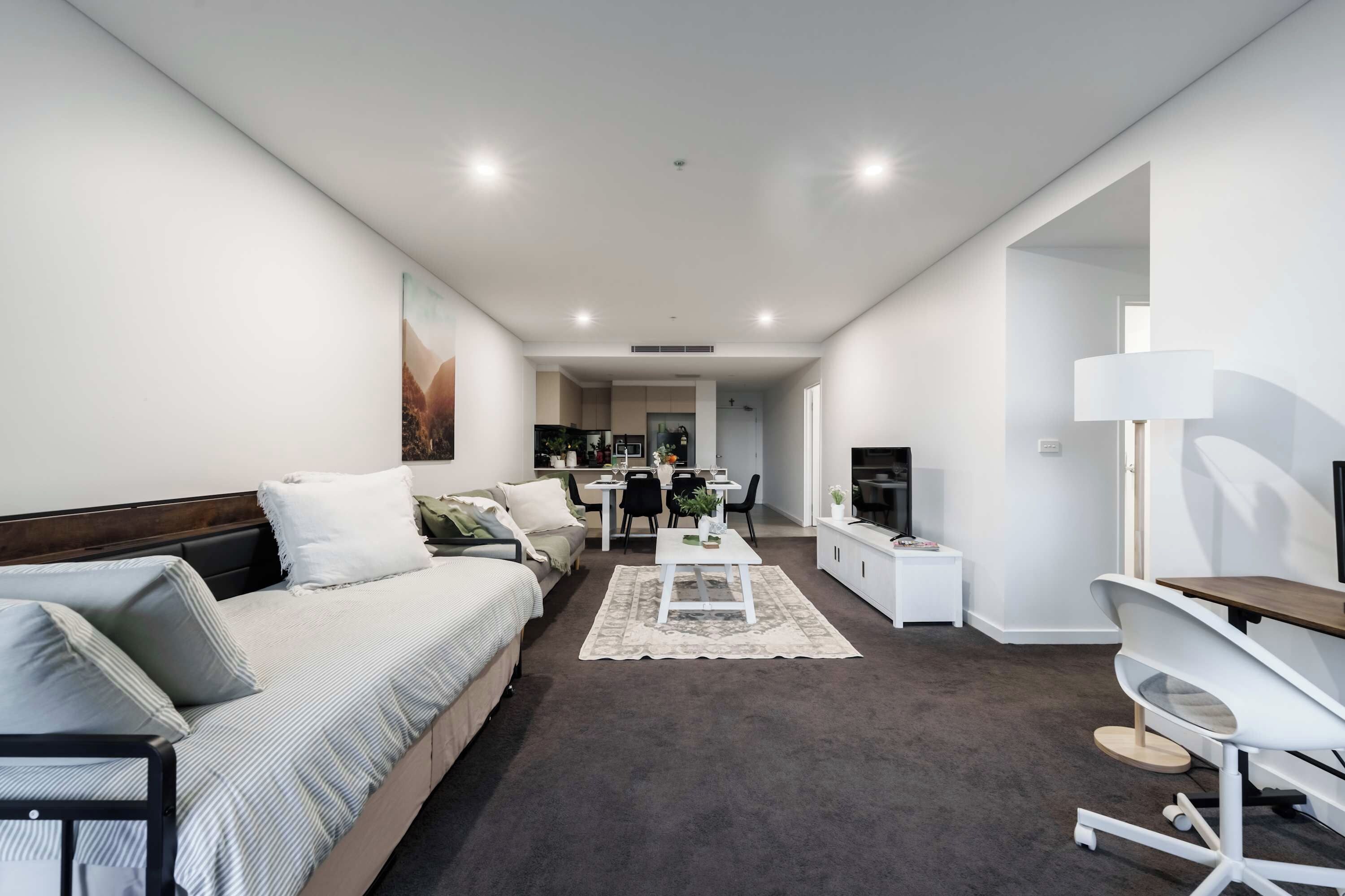 A modern, well-lit living room with a sofa, a dining area, and a TV.