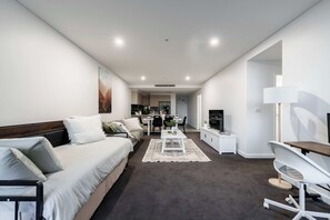 A modern, well-lit living room with a sofa, a dining area, and a TV. - Spiritus | Mountain View | Parking | Central (Wollongong)