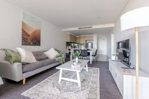 Ein modernes Wohnzimmer mit einem grauen Sofa, einem weißen Couchtisch und einem Essbereich im Hintergrund.
