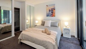 Una camera da letto con un letto, comodini, uno specchio e un quadro appeso al muro.