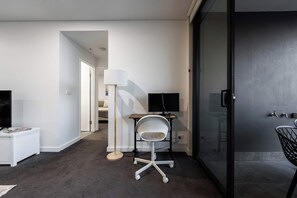 Moderni hotellihuone, jossa on taulutelevisio, työpöytä tuolilla, lamppu ja liukuovi.