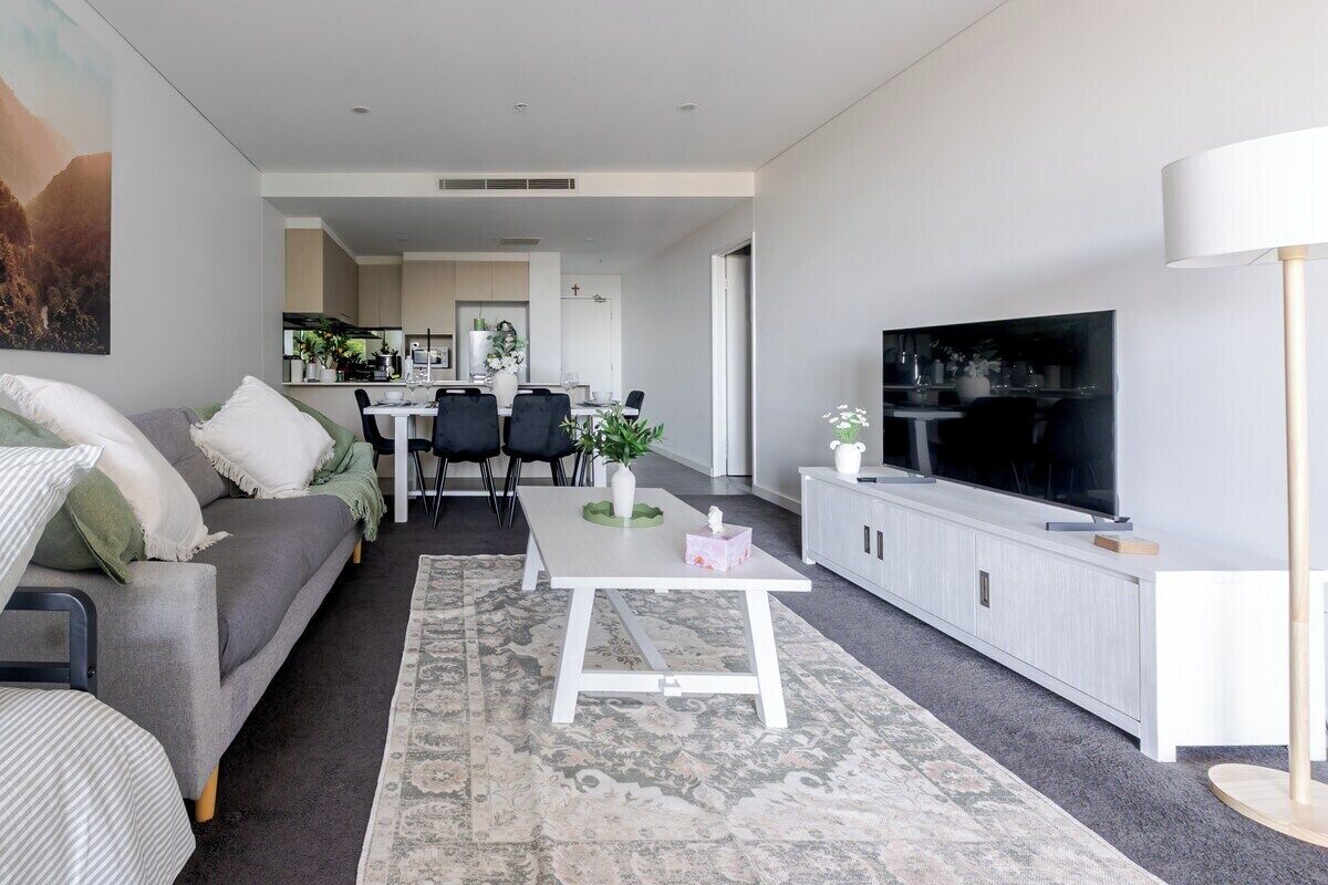 Een moderne woonkamer met een bank, een salontafel, een televisie en een eethoek op de achtergrond.