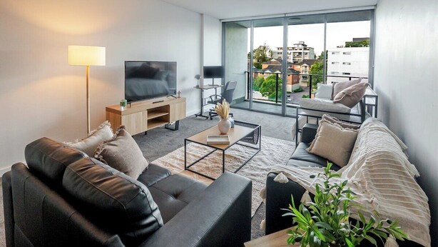 A modern living room with a black leather sofa, a wooden coffee table, and a large flat-screen TV. - Filioque | Mountain View | Parking | Central (Wollongong)