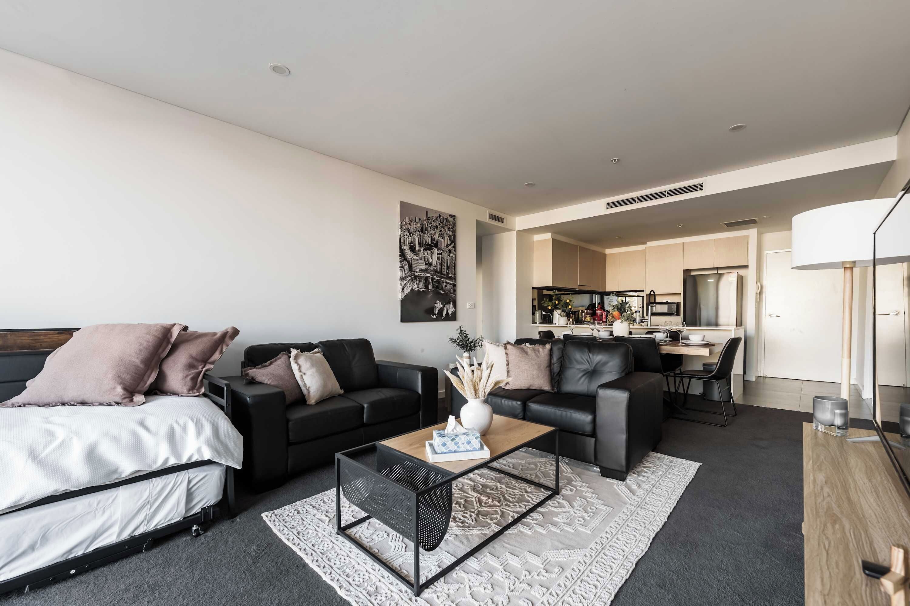 Een moderne woonkamer met een bed, twee banken, een salontafel en een keuken op de achtergrond.