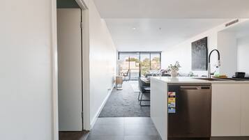 A modern kitchen with a dishwasher, a dining area with a table and chairs, and a view of the outdoors through large windows.