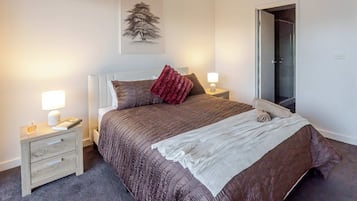 Un dormitorio con cama, mesitas de noche, lámpara, espejo y una obra de arte en la pared.
