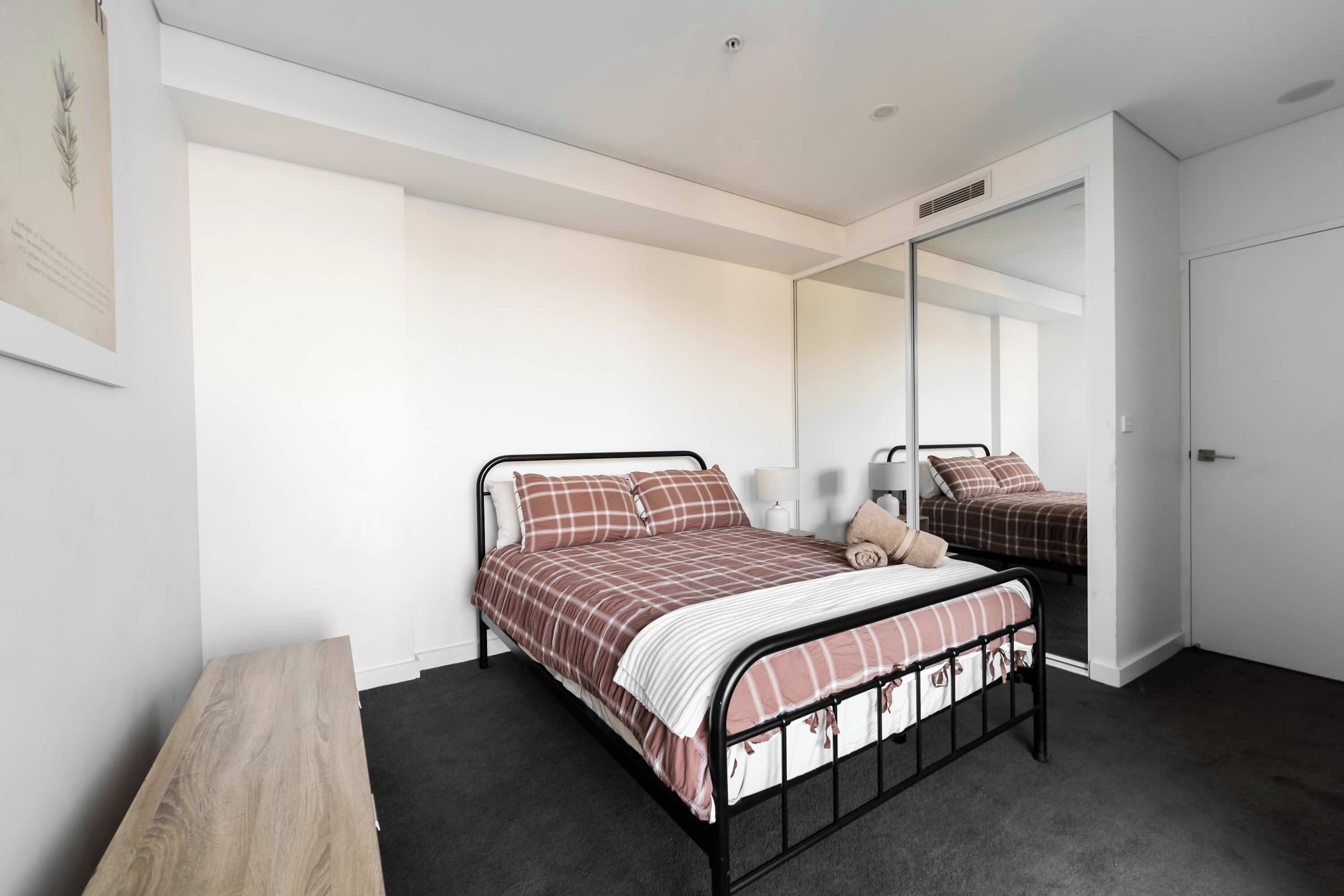 Een slaapkamer met een enkel bed, een nachtkastje, een spiegel en een kledingkast.