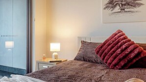A neatly made bed with a brown textured blanket, a red throw pillow, and a lamp on a bedside table. - Filioque | Mountain View | Parking | Central (Wollongong)