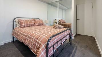 Una cama individual con estructura metálica y colcha escocesa en una habitación con un espejo grande y una puerta.