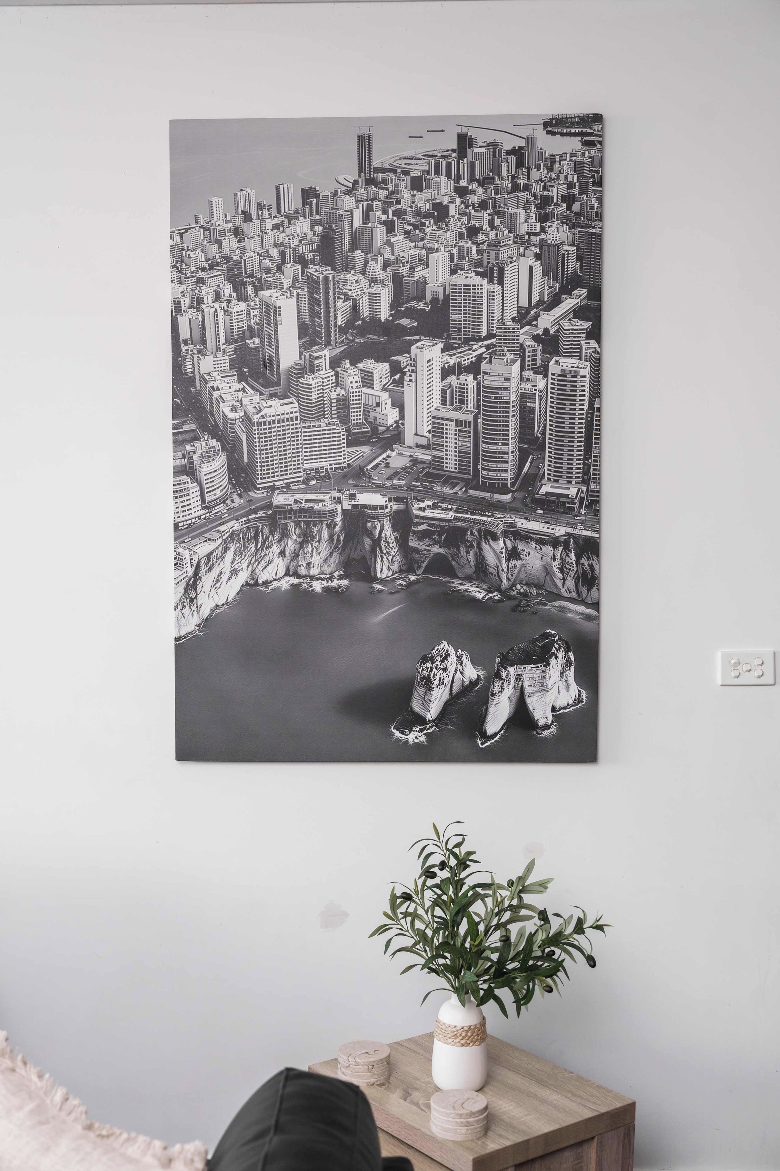 A black and white cityscape artwork on a wall, a small potted plant on a wooden table, and a white switchboard.