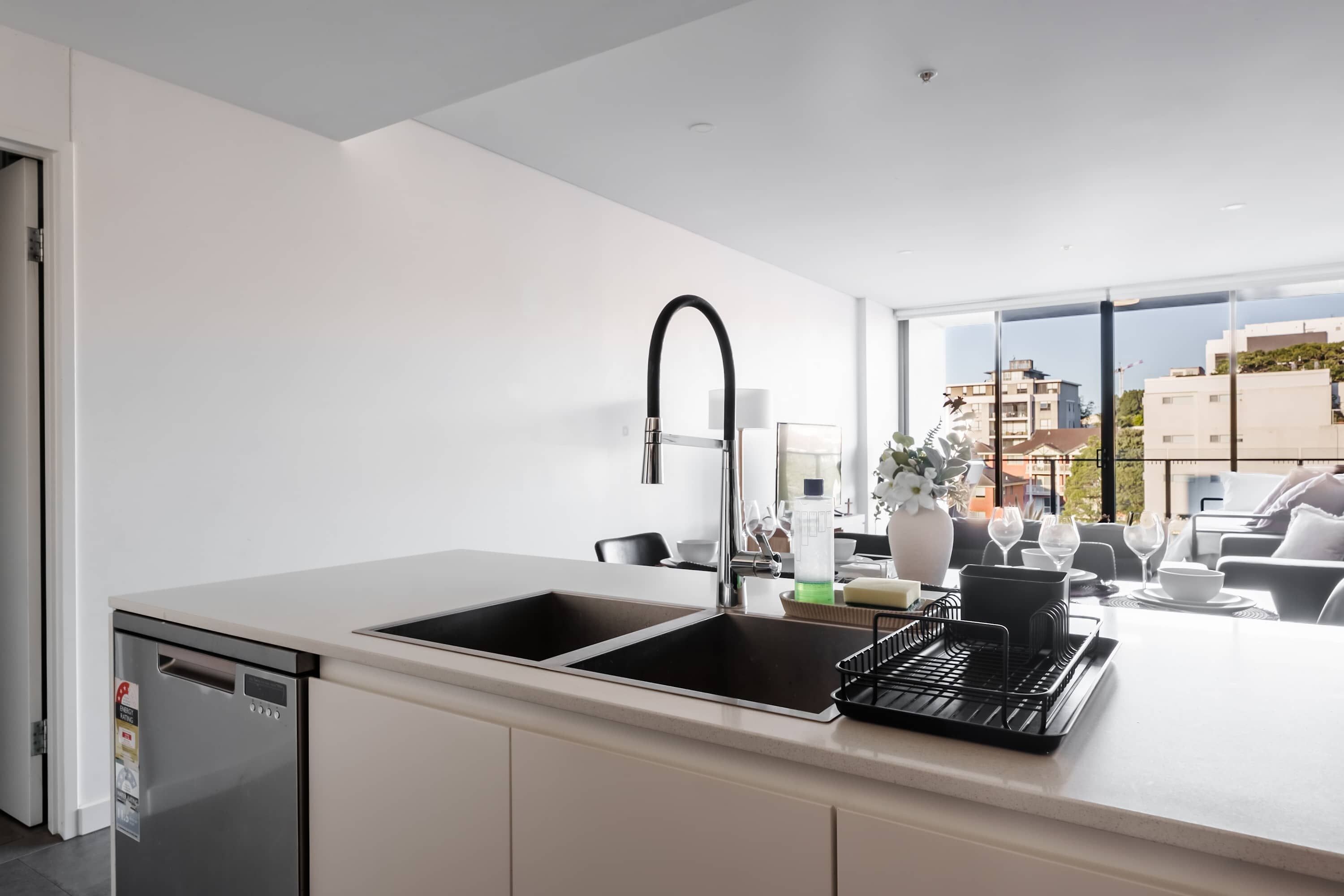 Een moderne keuken met een dubbele spoelbak, een vaatwasser en een groot raam met uitzicht op de stad.
