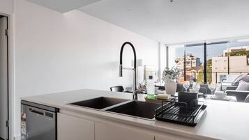 Een moderne keuken met een dubbele spoelbak, een vaatwasser en een groot raam met uitzicht op de stad.