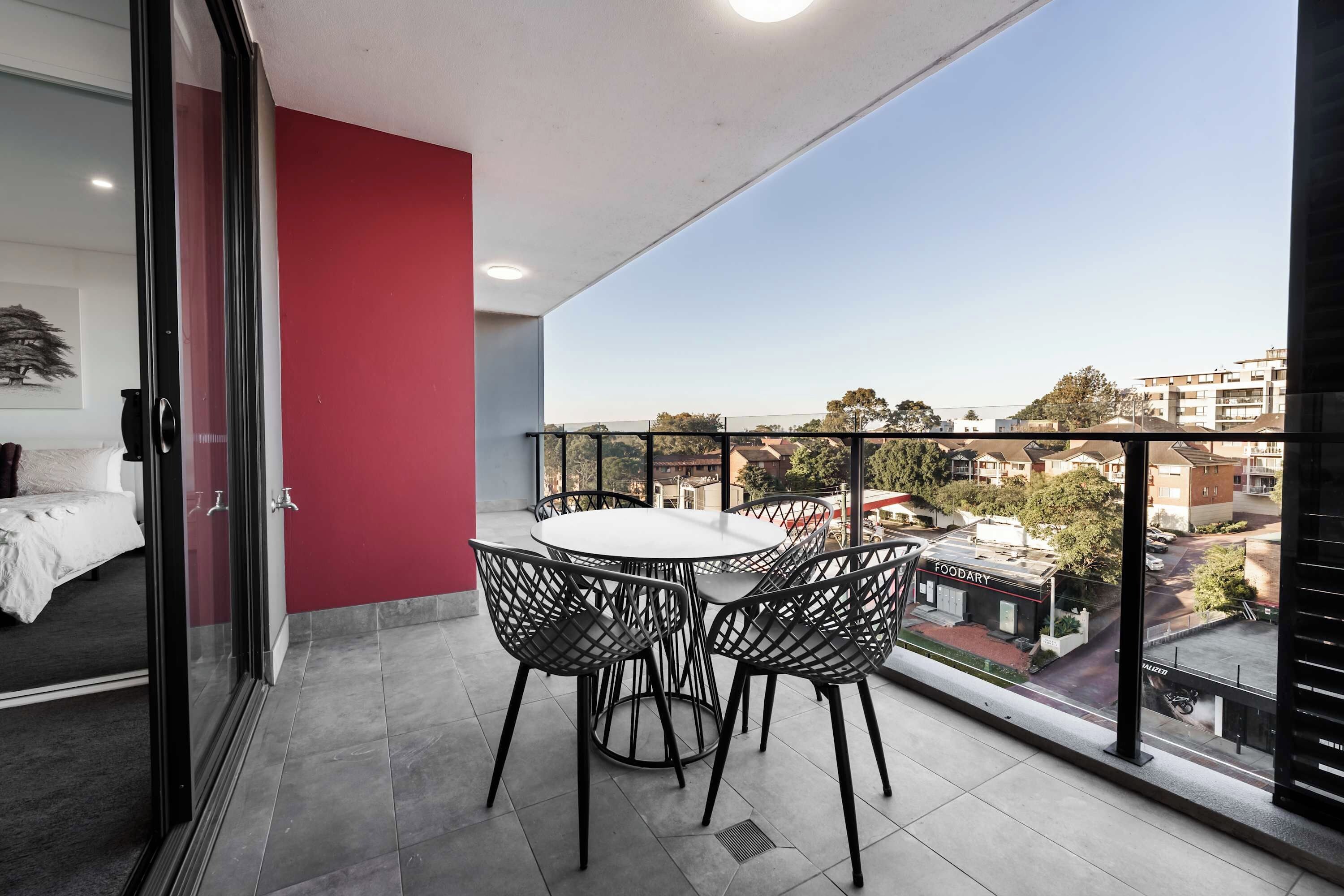 Ein Balkon mit Esstisch und Stühlen, einem Bett und einer roten Wand.