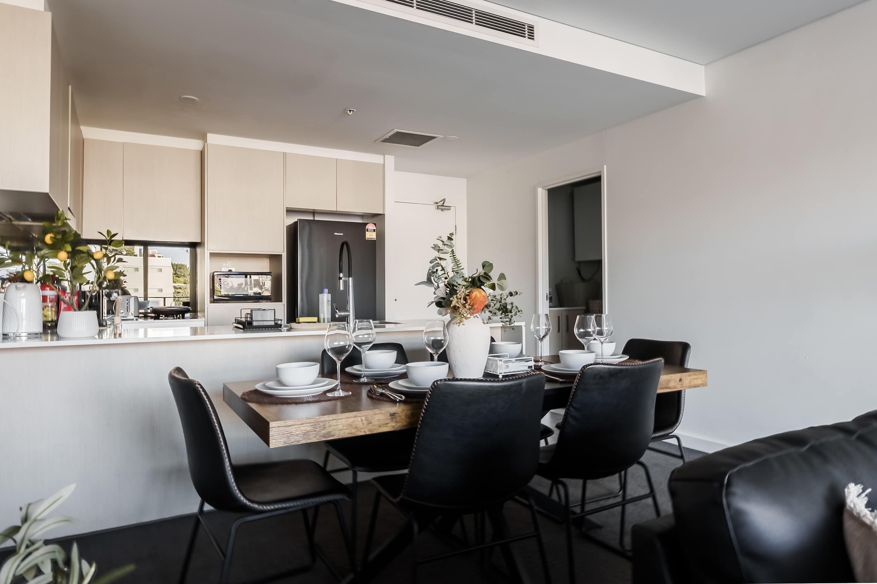 Cocina moderna con zona de comedor, que incluye un refrigerador negro, armarios blancos y una mesa de comedor con sillas.