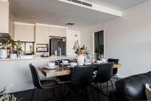 A modern kitchen with a dining area, featuring a black refrigerator, white cabinets, and a dining table set with chairs. - Filioque | Mountain View | Parking | Central (Wollongong)