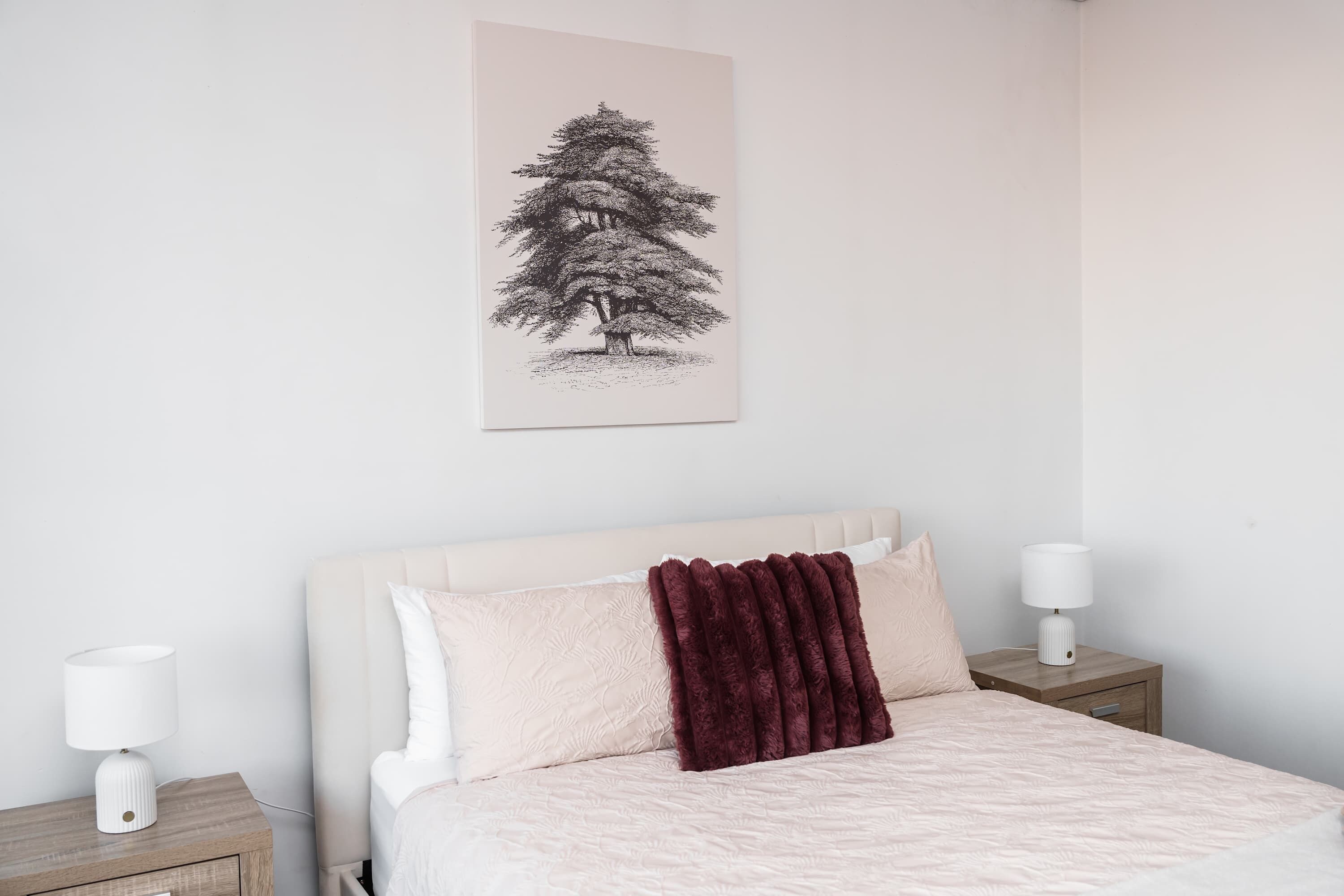 Un dormitorio con una cama, dos mesitas de noche, una lámpara y un cuadro en la pared.