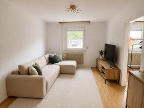 Una sala de estar moderna con un sofá modular, un televisor sobre un mueble de madera y una ventana con vistas al exterior.