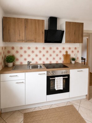 Cocina con armarios de madera, extractor de aire negro, pileta de acero inoxidable y salpicadero de azulejos.