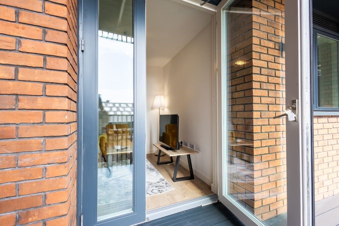 A modern interior with a sliding glass door leading to a balcony, a flat-screen TV, and a lamp on a small table.