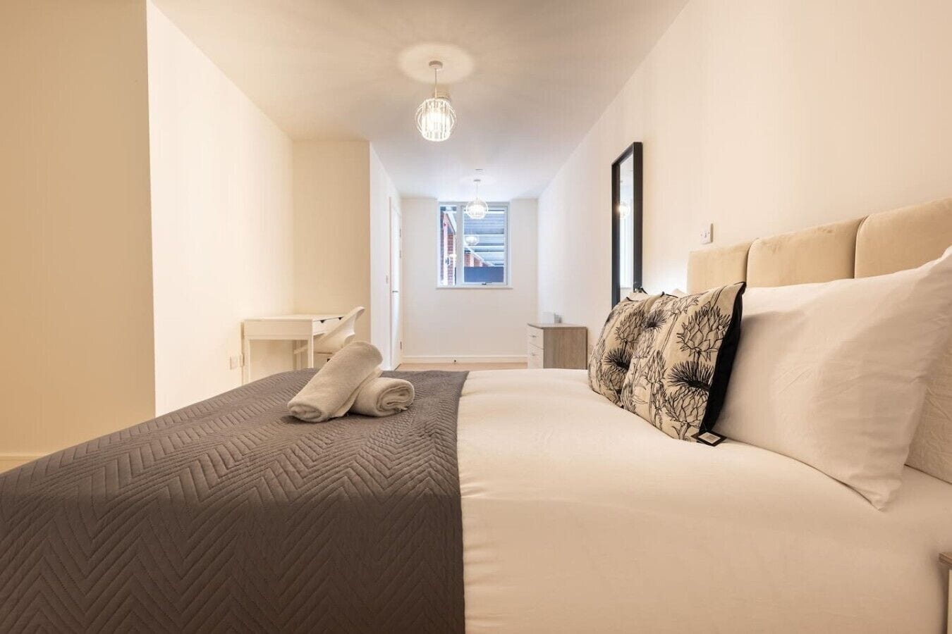 A hotel room with a bed, a bedside table, a chair, a window, and a door.