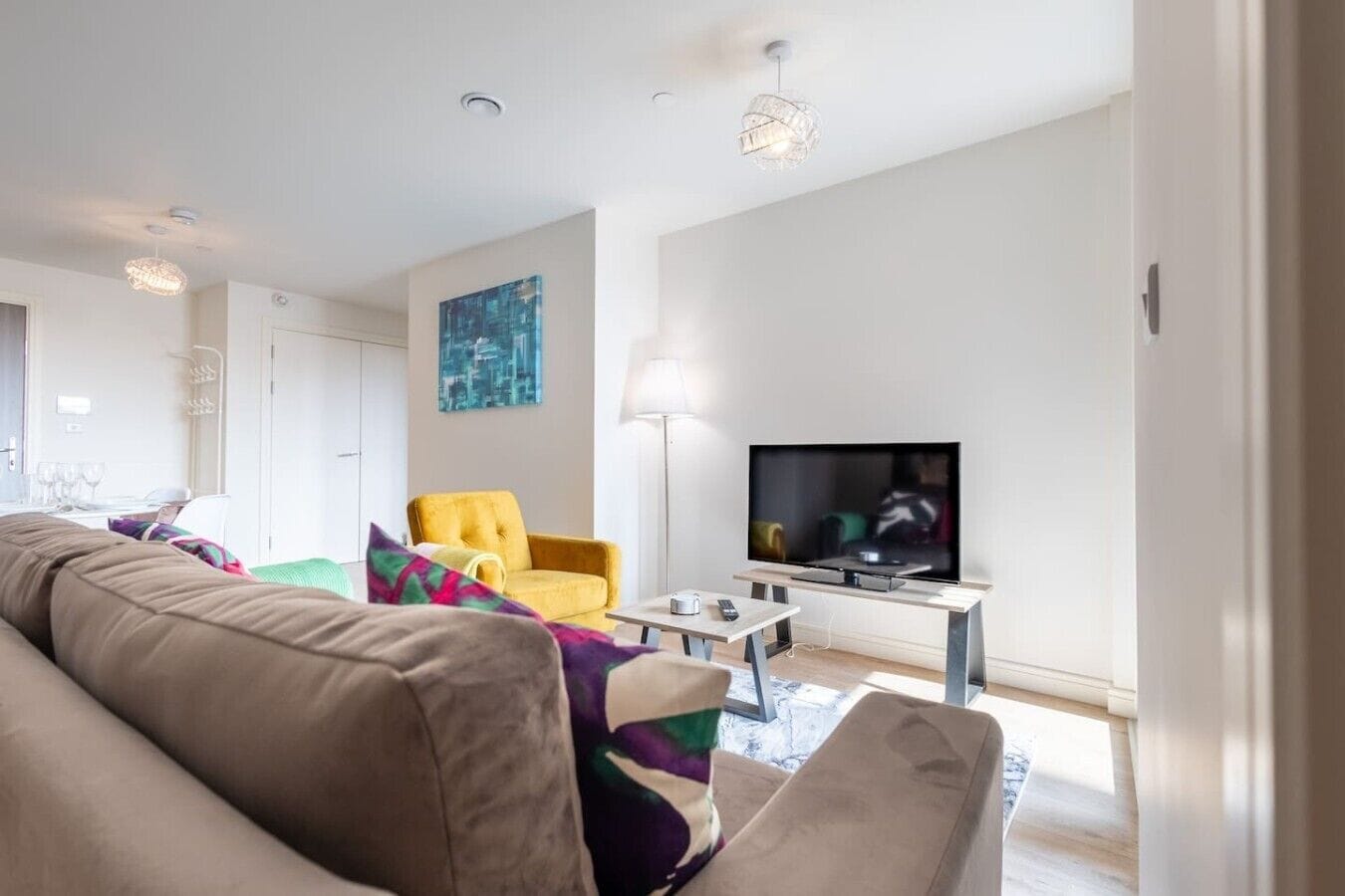 A modern living room with a sofa, a yellow armchair, a flat-screen TV, and a lamp.