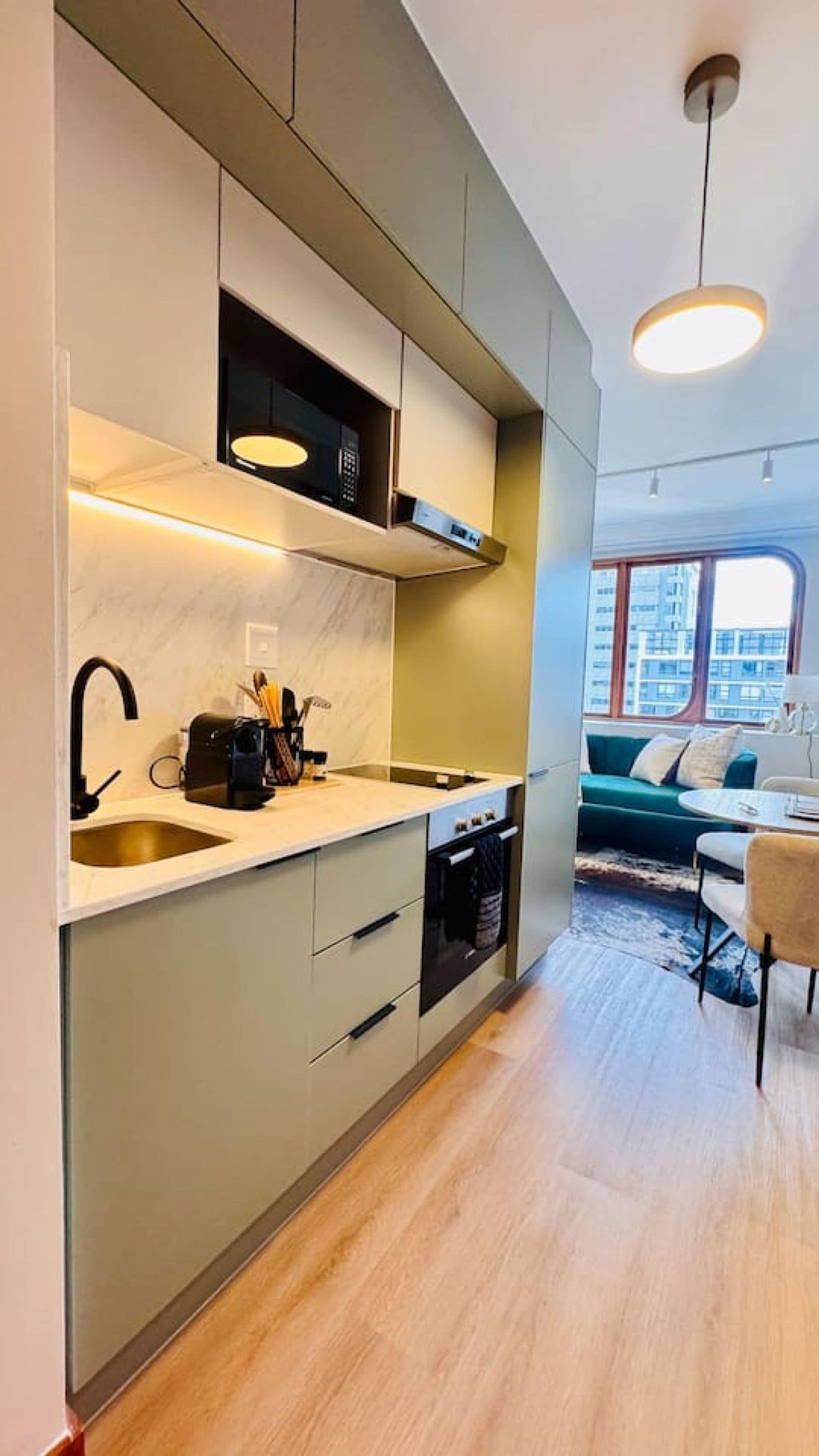 A modern kitchen with a built-in oven, a sink, and a microwave. There is a dining area with a table and chairs.