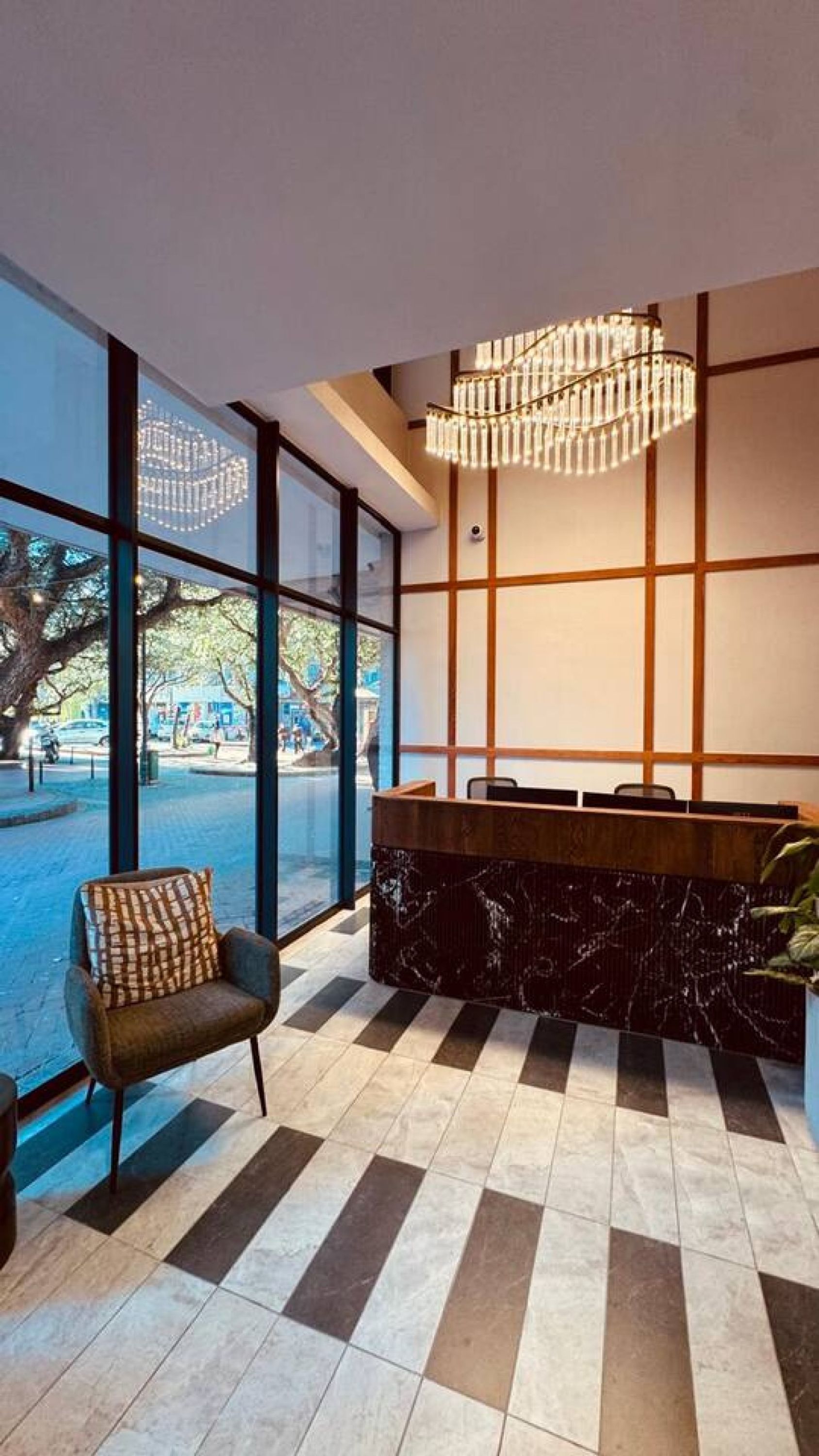 A reception area with a check-in counter, a seating area with a patterned chair, and large windows offering a view of the outdoors.