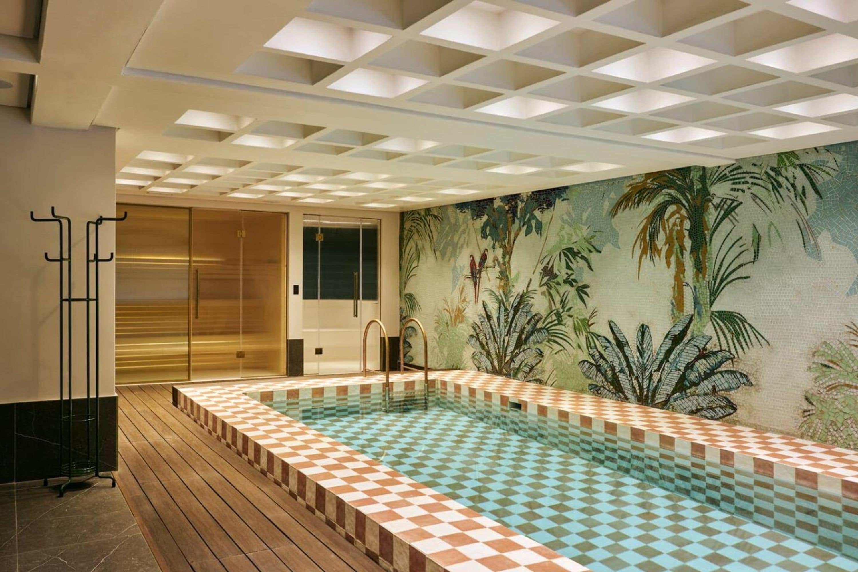 A swimming pool with checkered tiles, a wooden deck, and a mural of tropical plants on the wall.